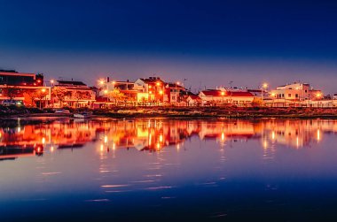 Kanalın suyunda yüzen teknelerle dolu gece manzarası.
