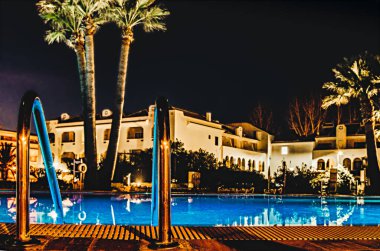 Havuzda palmiye ağaçları ve binalar olan gece yansımaları