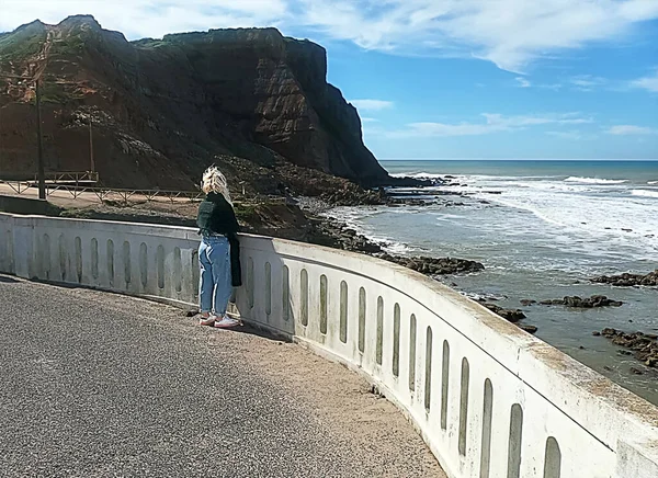 Blonde woman looking at the sea behind a concrete fence