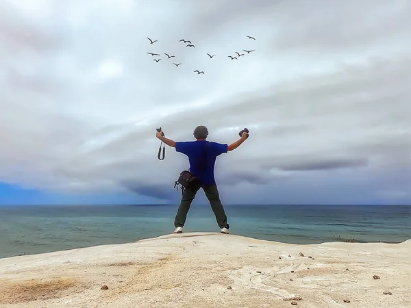 穿着蓝色T恤的男人在海边岩石边拍照 — 图库照片