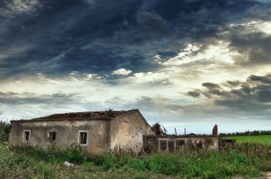 Tarlada terk edilmiş bir ev, dramatik bir gökyüzü.