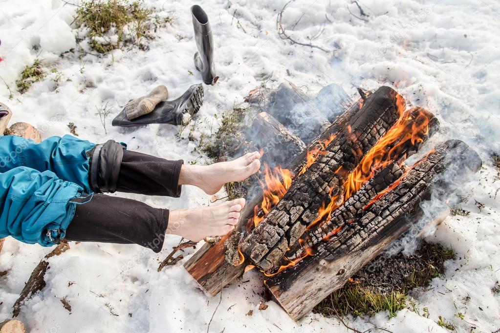 A man warms near the fire in the forest covered with snow 