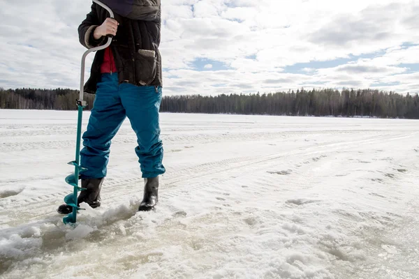 Ice fisherman drills using a bore on the lake — Stock Photo, Image