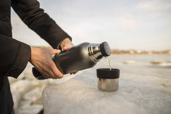 Man pours hot tea from a thermos into a cup