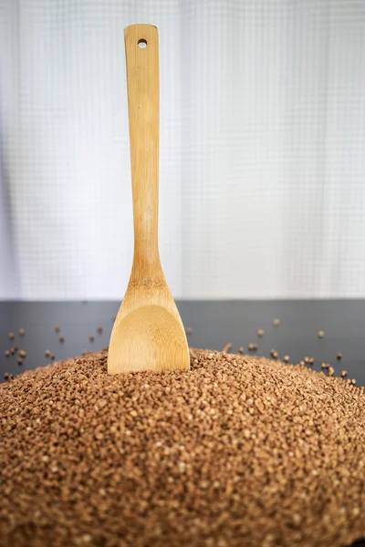 Montón de grañones de trigo sarraceno marrón sin cocer con cuchara de madera acostada —  Fotos de Stock