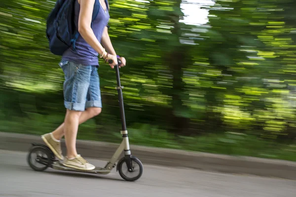 Hembra monta un scooter a velocidad por el camino, fondo borroso — Foto de Stock