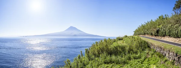 ถนนยางมะตอยใน Azores วิ่งไปตามชายฝั่งหญ้าของมหาสมุทรแอตแลนติก บนพื้นหลังของภูเขาไฟที่สูญพันธุ์ — ภาพถ่ายสต็อก