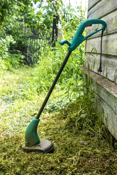 Cortador de césped eléctrico se encuentra en el jardín cerca de la casa —  Fotos de Stock