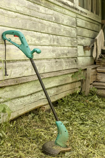Electric grass trimmer stands in the garden near the house — Stock Photo, Image