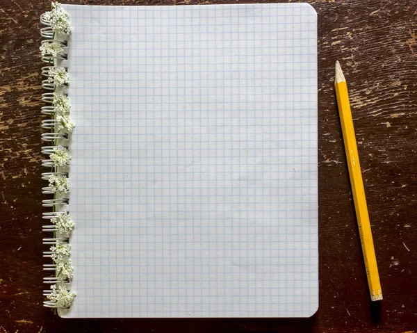 Notizbuch verziert mit kleinen weißen Blumen und einem Bleistift liegen auf dem Tisch. — Stockfoto