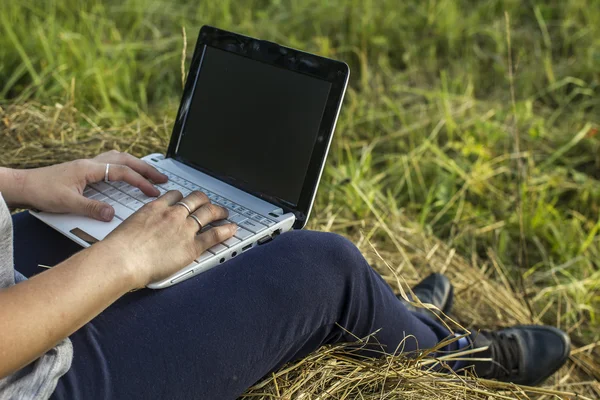 Mädchen arbeitet auf einem Laptop auf einem Heuhaufen in der Natur — Stockfoto