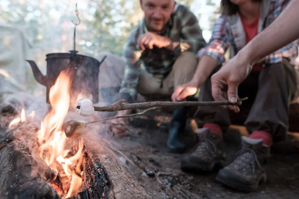 Groupe d'amis faire frire des guimauves sucrées au-dessus d'un feu, au-dessus de la flamme dont une bouilloire pend, dans un camp de camping, dans la forêt. — Photo