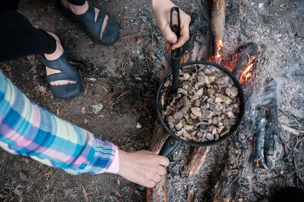 Faire frire les champignons sur un feu de camp dans une poêle. Les femmes préparent de la nourriture sur les charbons dans un camping, un jour d'été. Mode de vie. — Photo