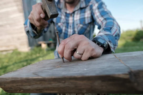 Le mani maschili di un falegname fanno una panchina martellando i chiodi in una tavola in un cortile del villaggio. — Foto Stock