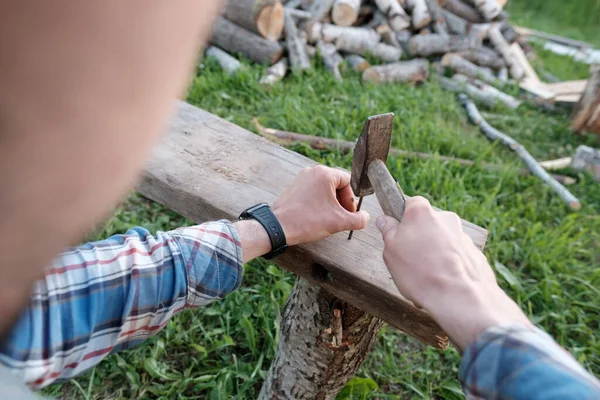 Le mani maschili di un falegname fanno una panchina martellando i chiodi in una tavola in un cortile del villaggio. Vista dall'alto. — Foto Stock