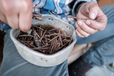 Bir marangozun erkek elleri plastik bir konteynırdan eski paslı çivileri seçer. Üst görünüm. 