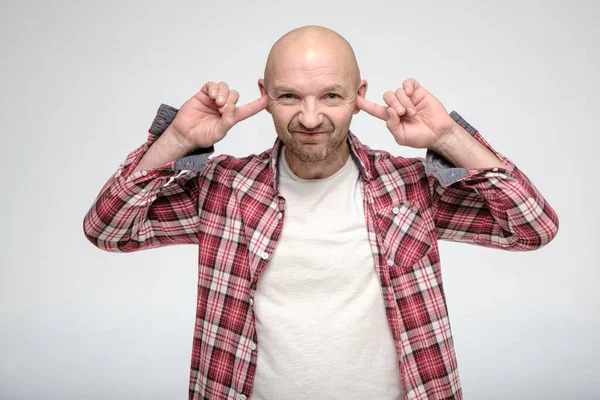 Caucasian bald, unshaven man covered ears with index fingers so as not to hear. — Stock Photo, Image