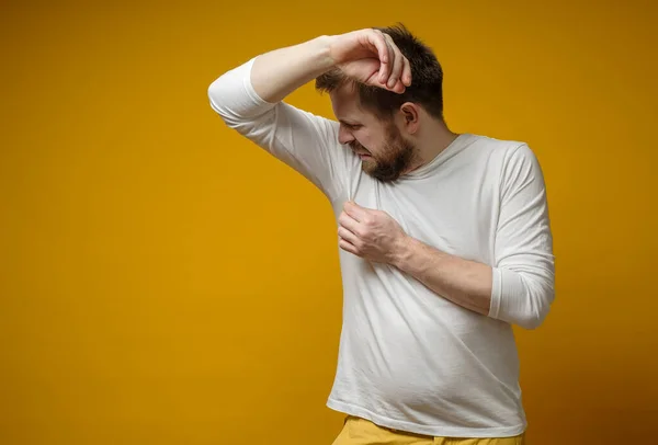 하얀 티셔츠를 입은 남자가 땀과 체취 문제로 짜증나는 자신의 겨드랑이에서 냄새를 맡는다. 복사 공간. — 스톡 사진