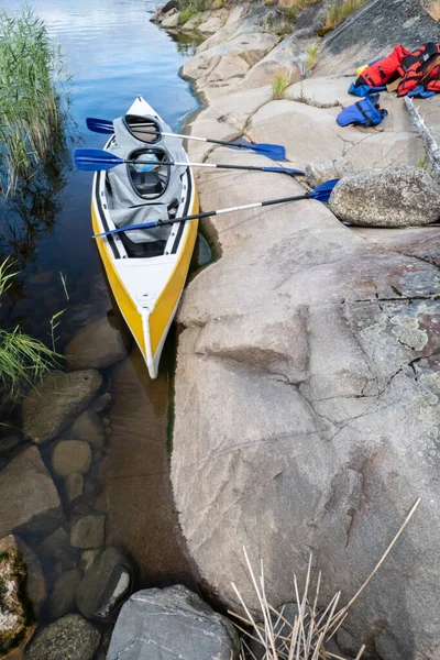 Three-seater kayak with paddles is parked on the rocky shore of the lake, on which life jackets lie. Leisure activities. — Stock Photo, Image