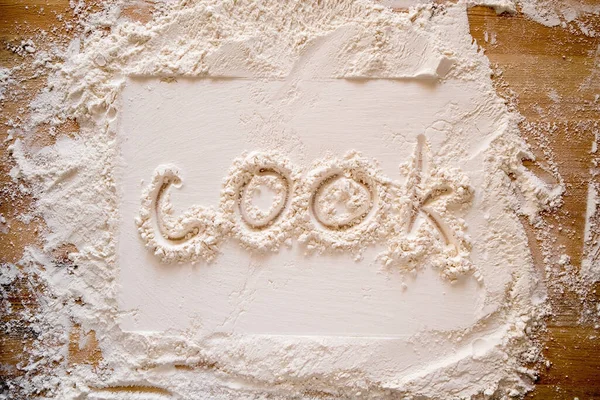 The handwritten word cook is written on flour sprinkled on a wooden table and a rectangular print. — Stock Photo, Image