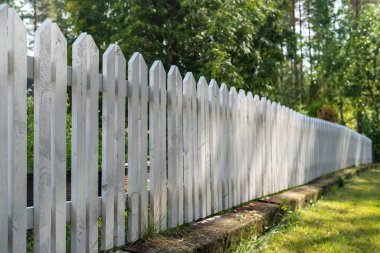 Bahçede beyaza boyanmış ahşap çitler, özel bölgelere erişimi yasaklıyor, ağaçların arka planına karşı..