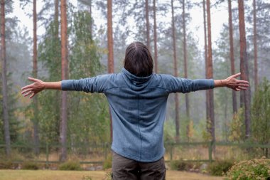 Mutlu kadın kollarını yana açmış ve sıcak yağmurun tadını çıkararak çam ormanını seyrediyor. Doğayla birlik. 