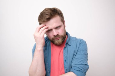 Canı sıkkın, beyaz bir adam elini yüzüne uzatıyor ve öfkeyle kameraya bakıyor. Beyaz arkaplan.