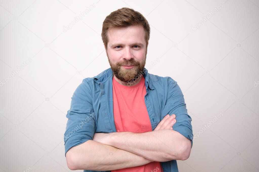 An attractive Caucasian man with a benevolent appearance stands with crossed arms and looks into the camera. White background.