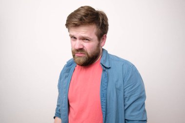 Beyaz sakallı adam güvensizce ve küçümseyici bir şekilde kameraya bakıyor. Beyaz arkaplan.