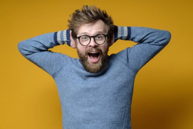 Mutlu, şaşırmış bir adam ellerini başının arkasında tutarken sevinçten çığlık atar. Sarı arkaplan.