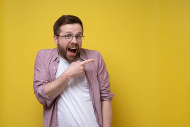 Şaşkın, pembe gömlekli ve gözlüklü yakışıklı adam parmağıyla kamerayı işaret ediyor. Boşluğu kopyala. 