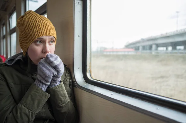 Sad woman rides on the train. She is cold and warms her gloved hands with her breath, looking thoughtfully out the window.