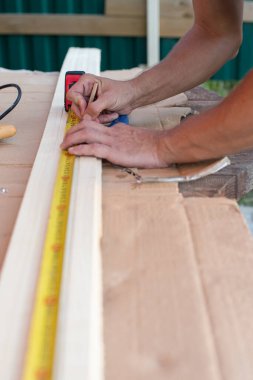 Marangoz elleri tahta bir tahta üzerinde mezura ile ölçü alır ve gerekli uzunluğu kalem ile işaretler..