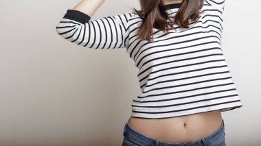 Kendine güvenen kot pantolonlu ve çizgili kazaklı bir kız kollarını kaldırdı ve güzel göbeğini ve ince belini uzattı. Boşluğu kopyala.