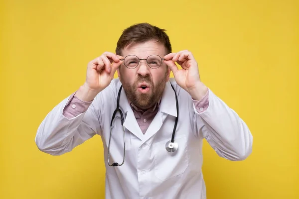 Gözleri iyi görmeyen komik bir doktor, elinde gözlüklerle bir şeyler görmeye çalışır, yüzünde şaşırmış bir ifade vardır.. — Stok fotoğraf
