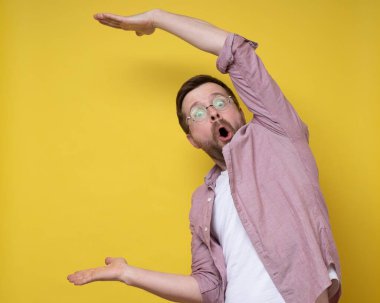 Gözlüklü şaşırmış bir adam elleri olan büyük bir adam gösteriyor. Abartıyor ve hayret içinde kameraya bakıyor. Boşluğu kopyala. 