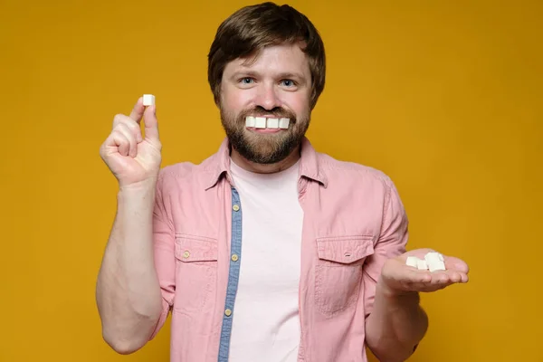 O homem engraçado pôs pedaços de açúcar na boca como se fossem dentes e sorrisos. Fundo amarelo. — Fotografia de Stock