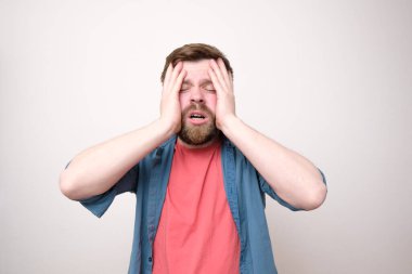 Yorgun ve stresli sakallı bir adam ellerini başının üstüne koyar ve gözlerini kapatır. Depresyon. Baş ağrısı problemleri. Beyaz arkaplan.