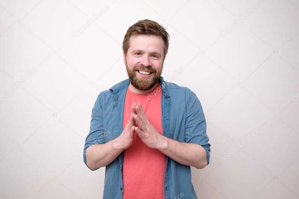 Smiling bearded man calmly and confidently looking at the camera with palms together. Isolated, white background.