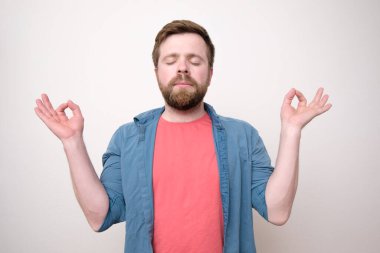 Çekici, sakin, sakallı, gözleri kapalı, meditasyon yapan ve uyum ve dengeyi bulmaya çalışan bir adam. Beyaz arkaplan.