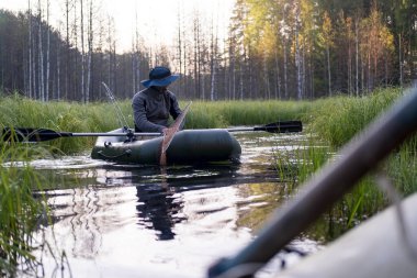 Şişme bir teknede şapkalı bir balıkçı şafakta göller arasındaki boğazda balık tutmaya hazırlanıyor..
