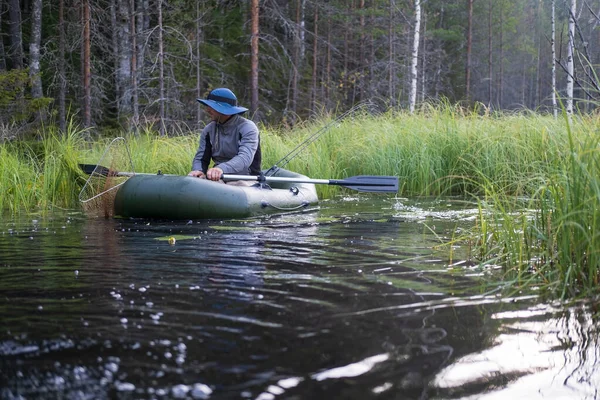 Visser in een hoed op een opblaasbare boot bereidt zich voor om te vissen in de rivier, bij dageraad, tegen de achtergrond van het bos. — Stockfoto