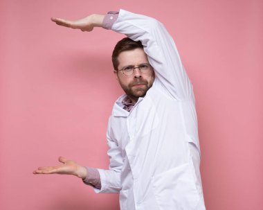 Yuvarlak gözlüklü ciddi bir doktor tuhaf bir poz veriyor ve kameraya sert bakıyor. Uzayı kopyala Pembe arkaplan.