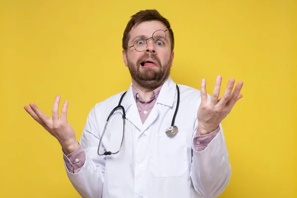 Yüzünde aptal bir ifade ve alnında gözlük olan kafası karışmış bir doktor elleriyle karışık bir jest yapıyor. Sarı arkaplan. — Stok fotoğraf