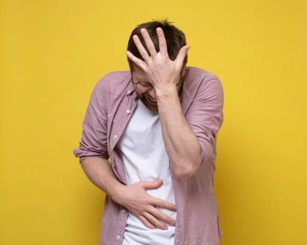 Der junge Mann hat sehr starke Bauchschmerzen, er leidet an Bauch- und Kopfschmerzen. Gelber Hintergrund. — Stockfoto