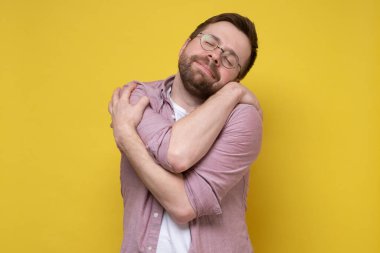 Sevimli, yuvarlak gözlüklü komik sakallı adam kendine sarılıyor, aşkı hayal ediyor ya da narsisizmden muzdarip, gözlerini kapatıp tatlı tatlı gülümsüyor.. 