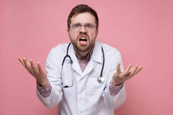 Woedend, verbaasd arts maakt een ondervraging en verbijsterd gebaar met handen en kijkt naar de camera. — Stockfoto