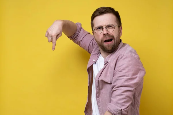 Bewildered man persistently points finger down and looks inquiringly at the camera with a strange expression on face. Copy space. — Stock Photo, Image