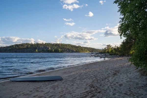 Sulla riva sabbiosa si trovano kayak rovesciati, sullo sfondo del lago e la riva rocciosa con alberi. Bellissimo paesaggio. — Foto Stock