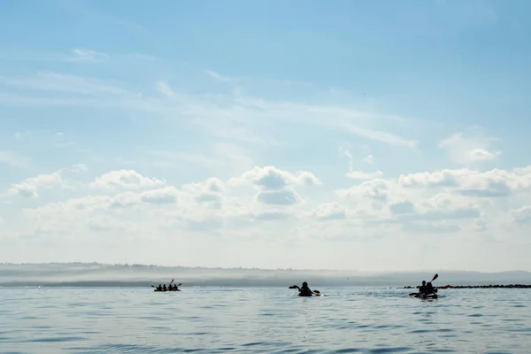 水平線に対して湖に浮かぶ観光客と3つのカヤックのシルエット。レジャー・スポーツ. — ストック写真